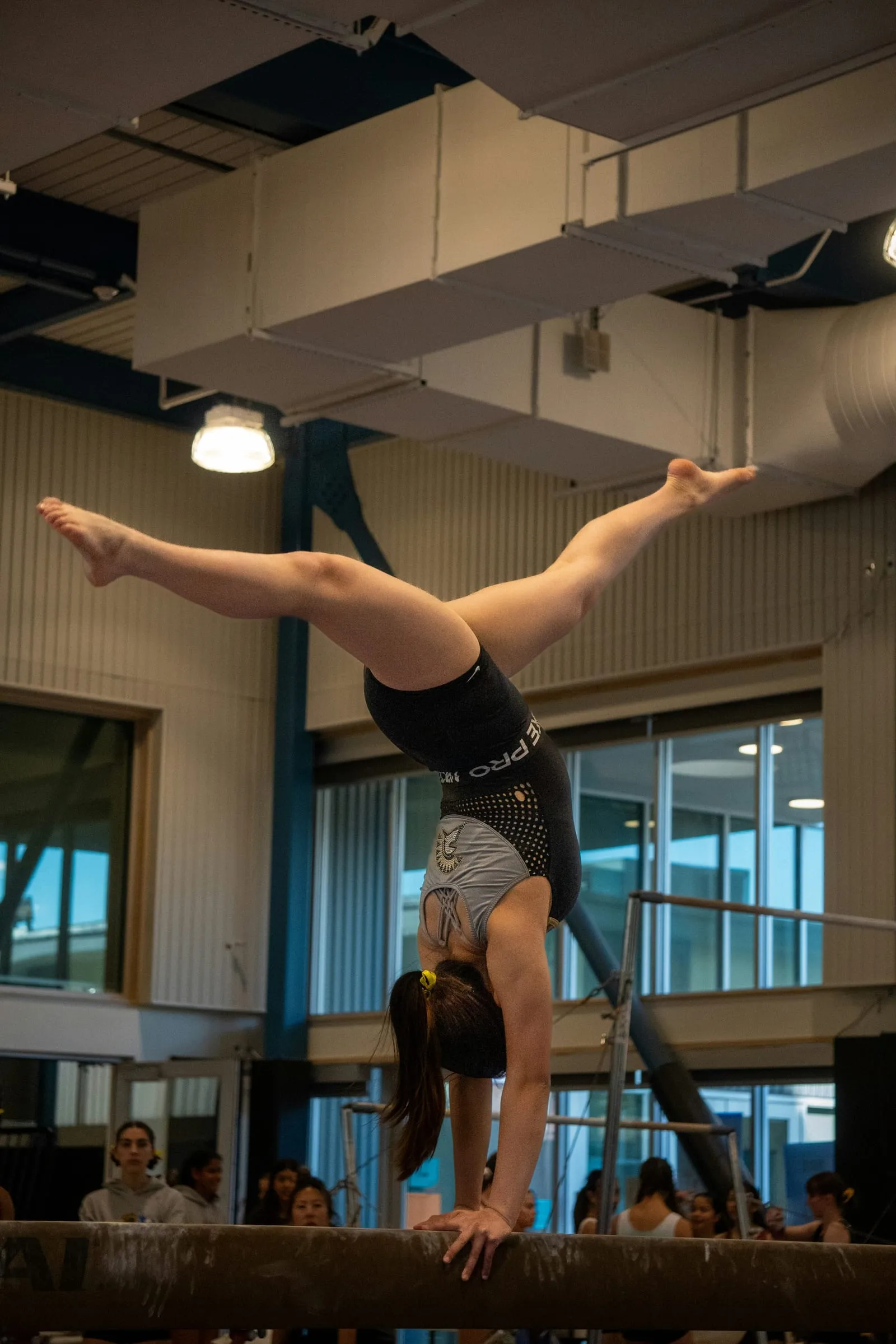 A gymnast holding a split handstand on a balance beam