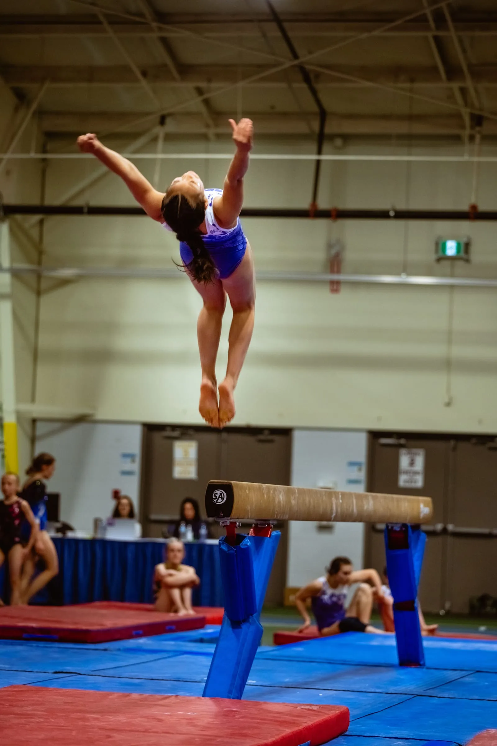 A gymnast in mid-air above a balance beam