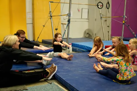 Two coaches leading a circle of preschoolers through a seated stretch